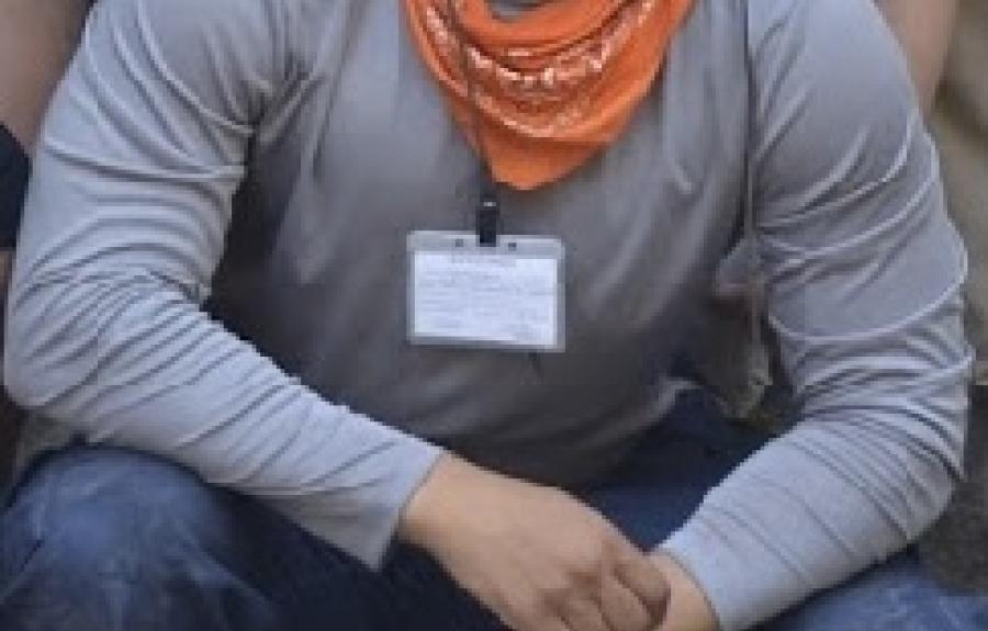 student Joshua Johnson kneeling and smiling at archaeology dig site 