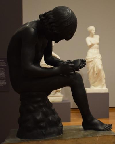 Statue of boy inspecting foot