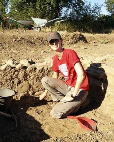 A students poses in a small pit of an archaeological dig